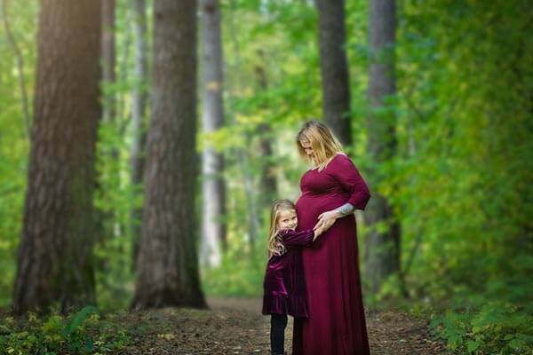 Gravid kvinna fotograferad i vacker skog med blivande syskonet kramandes den blivande mamman. av Studio-Li